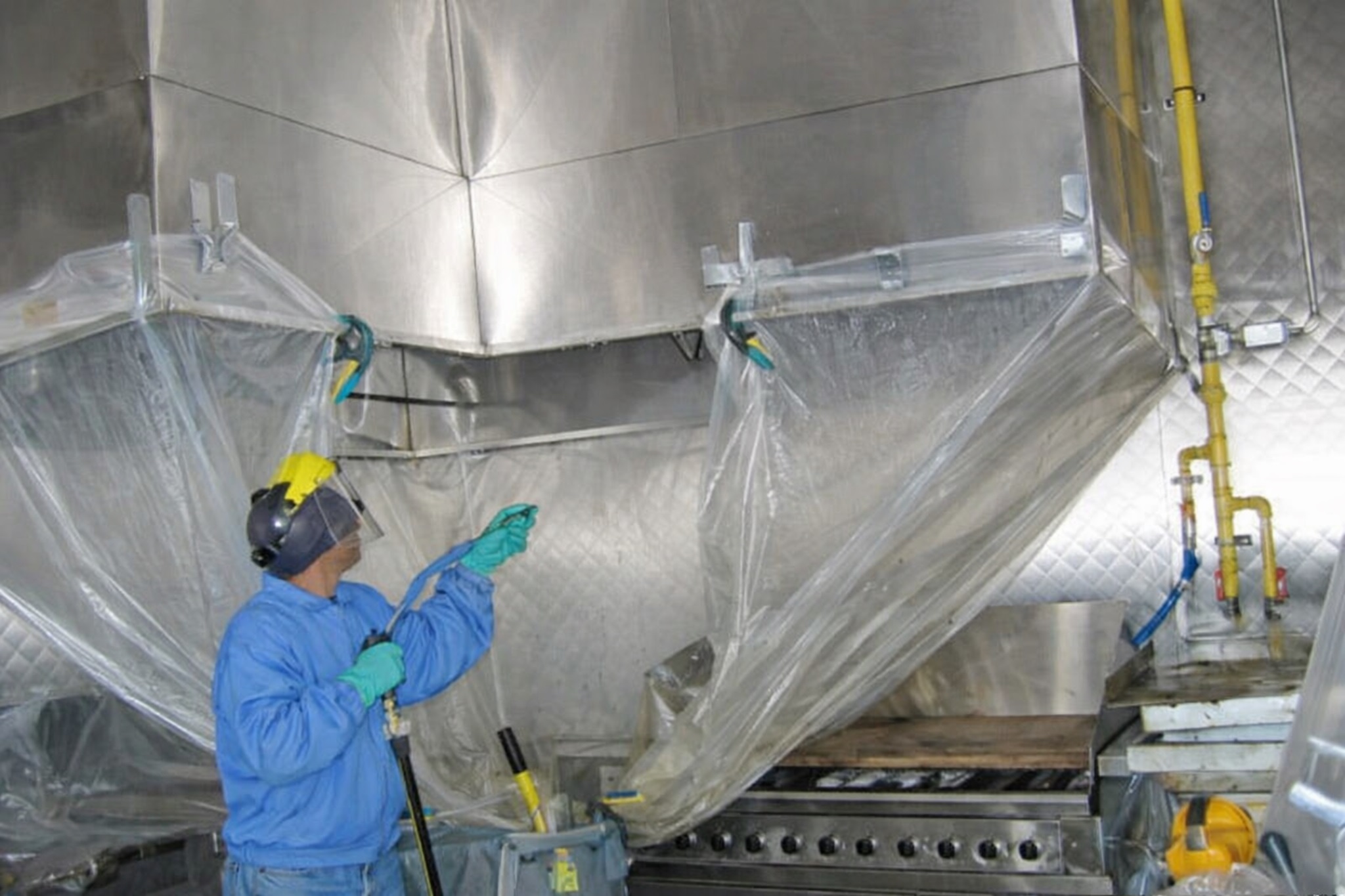 Technician degreasing commercial kitchen exhaust hood using hot water pressure washing in Virginia Beach